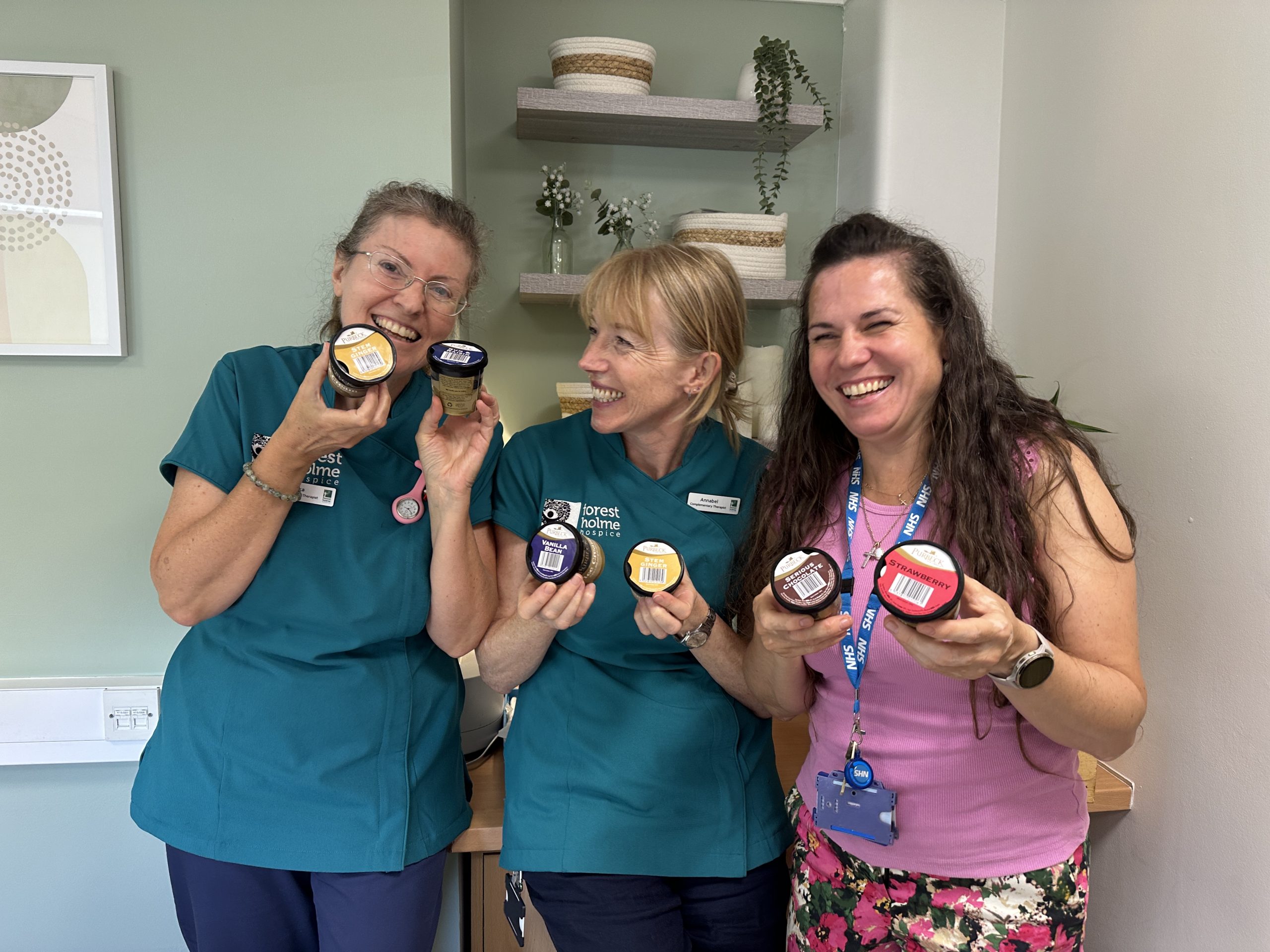 3 woman from Forest Holme Hospice with a Purbeck Ice Cream tub on their hands, smiling.